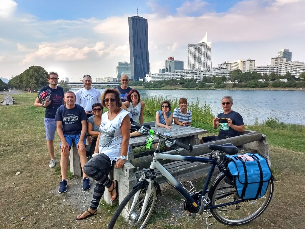 Cicloturisti lungo il Danubio a Vienna con skyline sullo sfondo, viaggio in bici tra natura e città