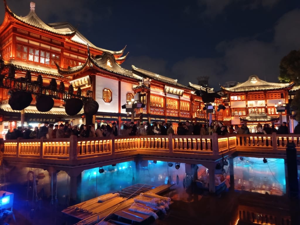 Yuyuan Bazaar a Shanghai di notte con edifici tradizionali illuminati e laghetto viaggio organizzato in Cina