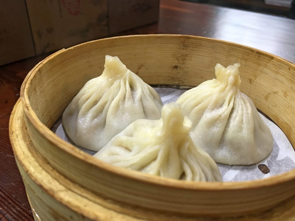 Cestino in bambù con ravioli al vapore cinesi xiaolongbao su tavolo da ristorante.