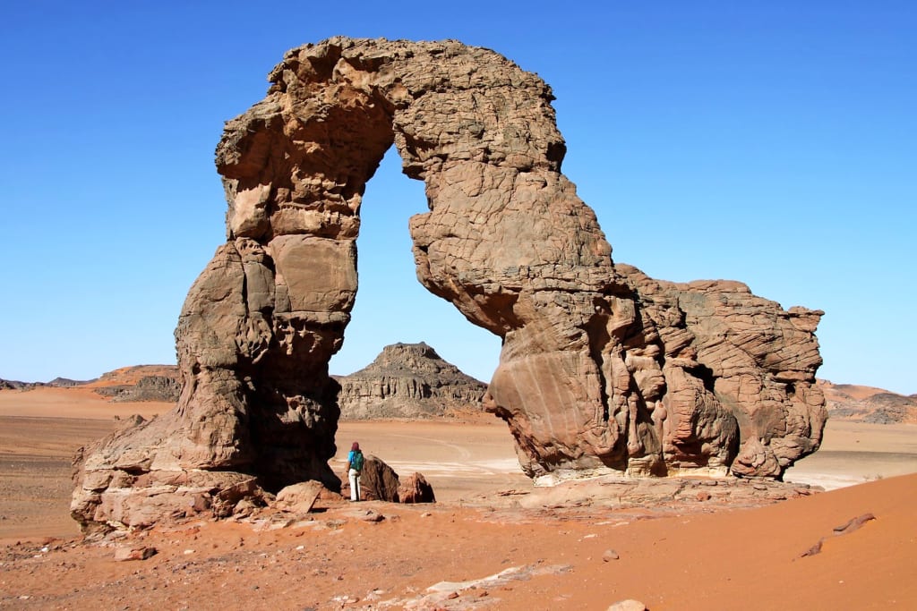 Formazione rocciosa naturale ad arco nel deserto del Sahara, circondata da paesaggi aridi e cielo limpido.