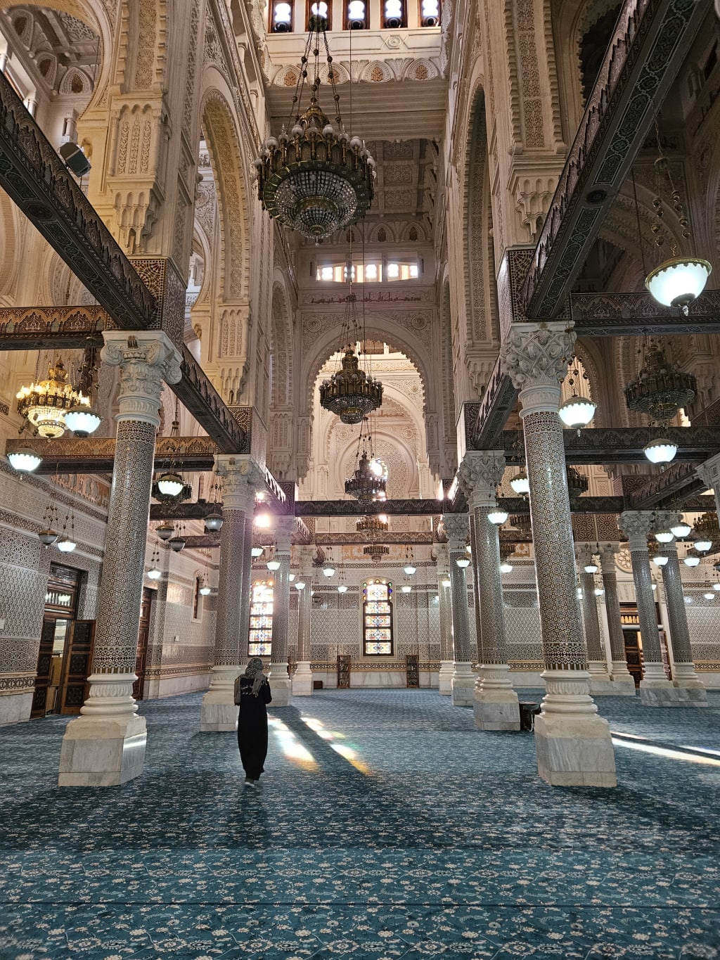 Interno della Grande Moschea di Algeri con dettagli architettonici maestosi, colonne e lampadari.