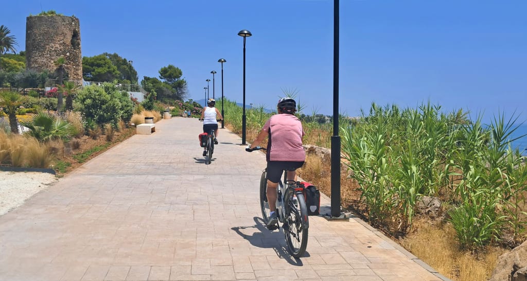 Cicloturisti su pista ciclabile lungomare in Andalusia, itinerario in bici tra spiagge e paesaggi mediterranei