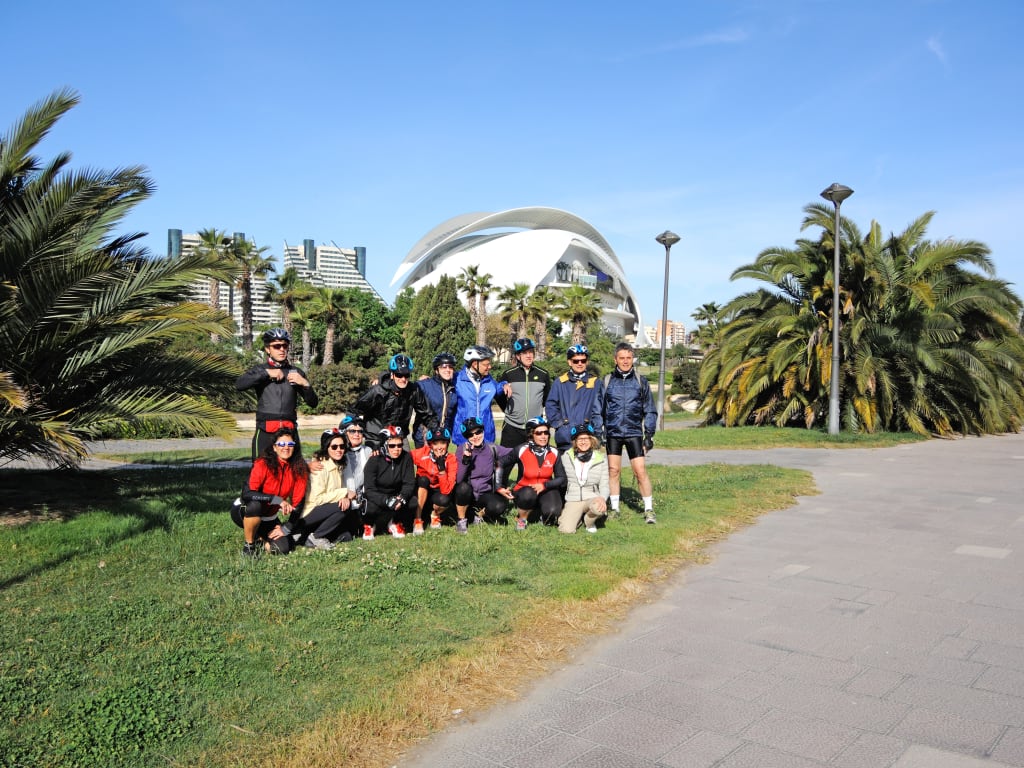 Gruppo di viaggiatori in bicicletta lungo pista ciclabile nel Parco del Turia a Valencia, viaggio attivo tra natura e città