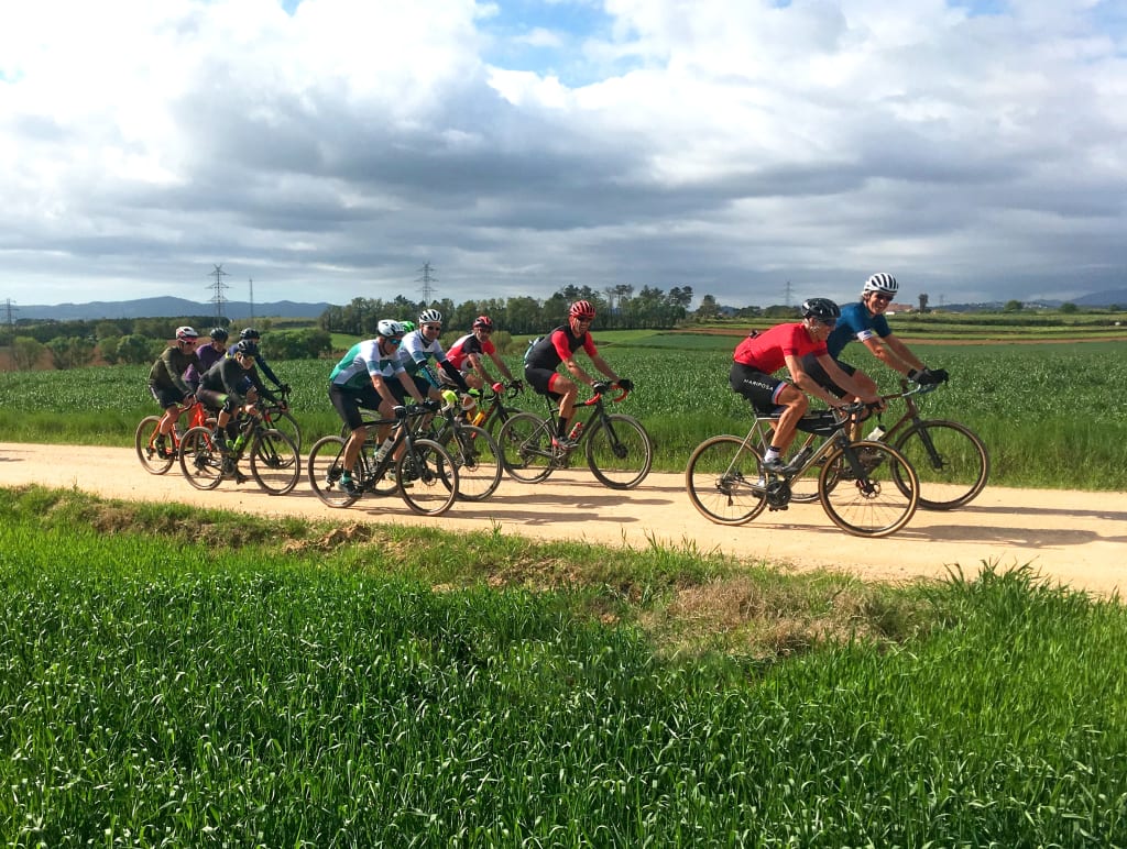 Gruppo di ciclisti su una strada panoramica collinare nella Catalogna, Spagna, con cielo nuvoloso.