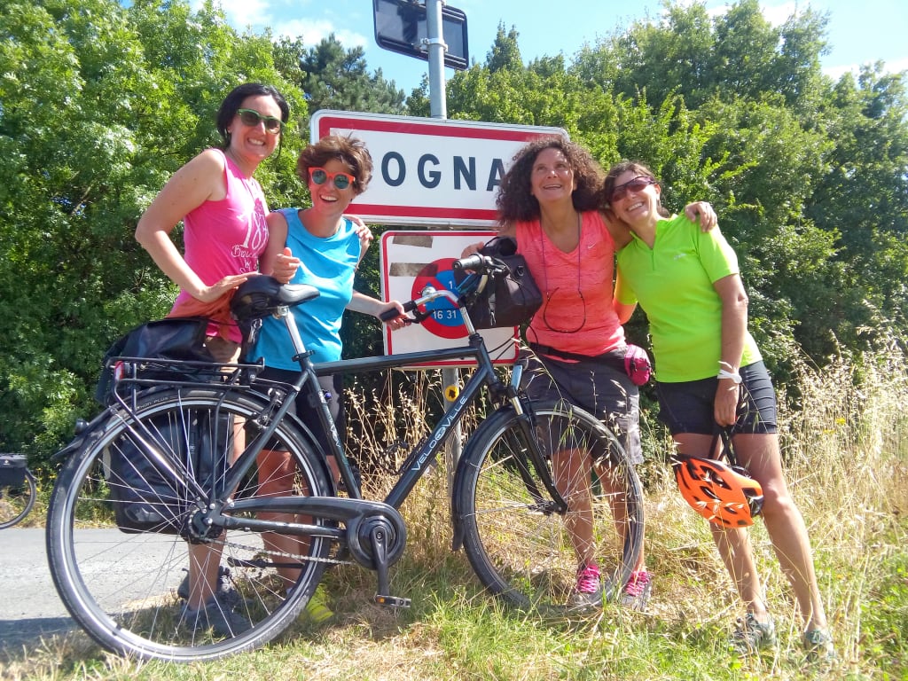 Cicliste sorridenti fanno una foto davanti a un cartello con la scritta "Cognac", vacanze di gruppo in bicicletta "Girolibero"