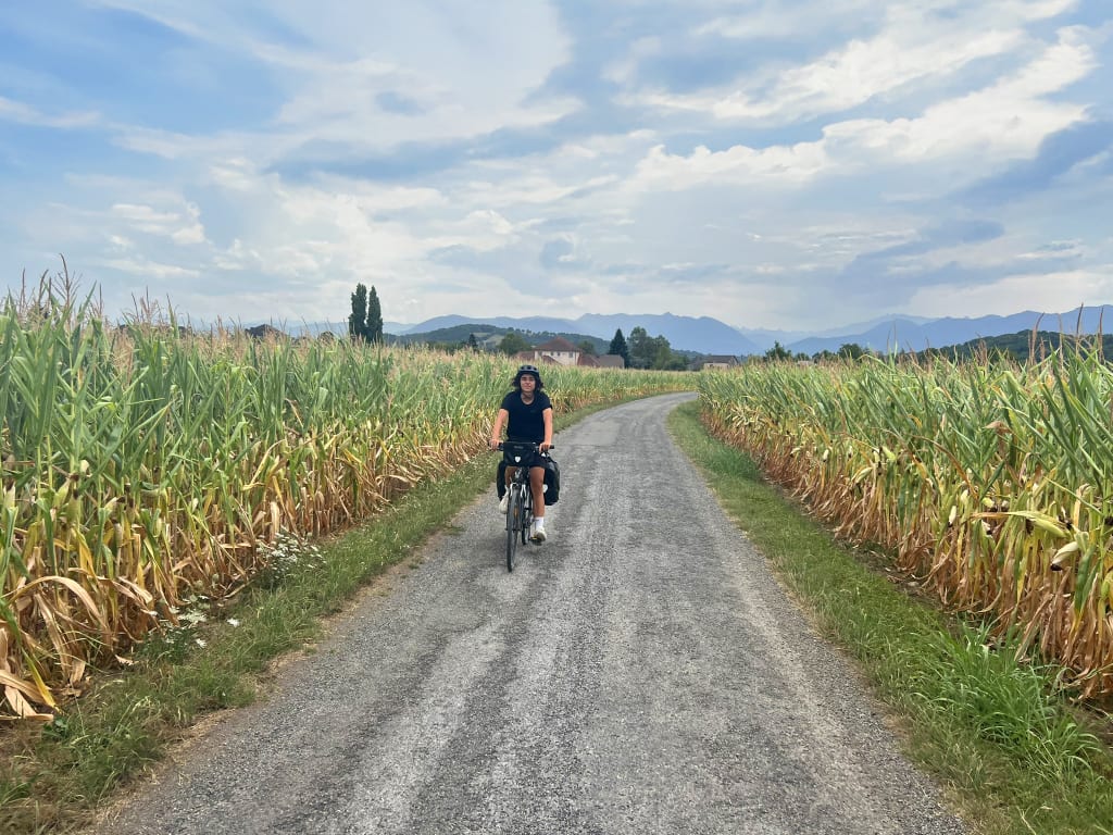 Ciclista su strada di campagna tra campi coltivati, viaggio in bicicletta nella Francia rurale