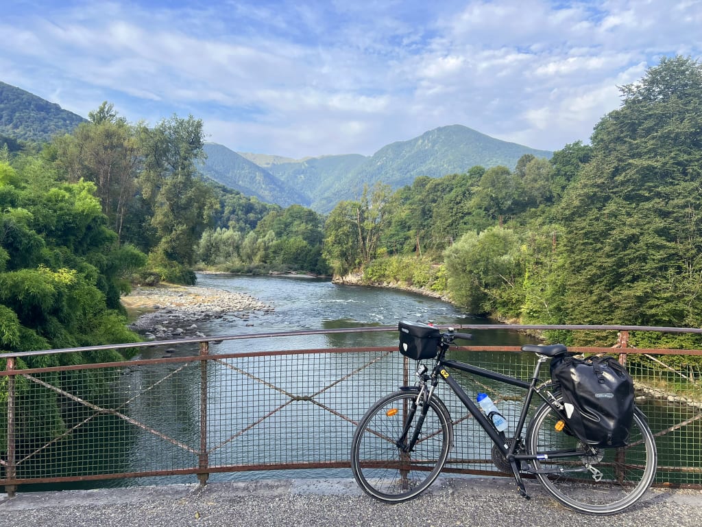 Fiume immerso nel verde della Vélosud con montagne sullo sfondo, paesaggio naturale attraversato durante un viaggio in bici
