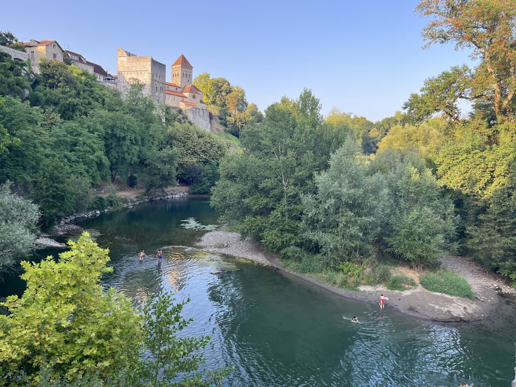 Fiume circondato da vegetazione con borgo storico sullo sfondo, paesaggio fluviale lungo un viaggio slow