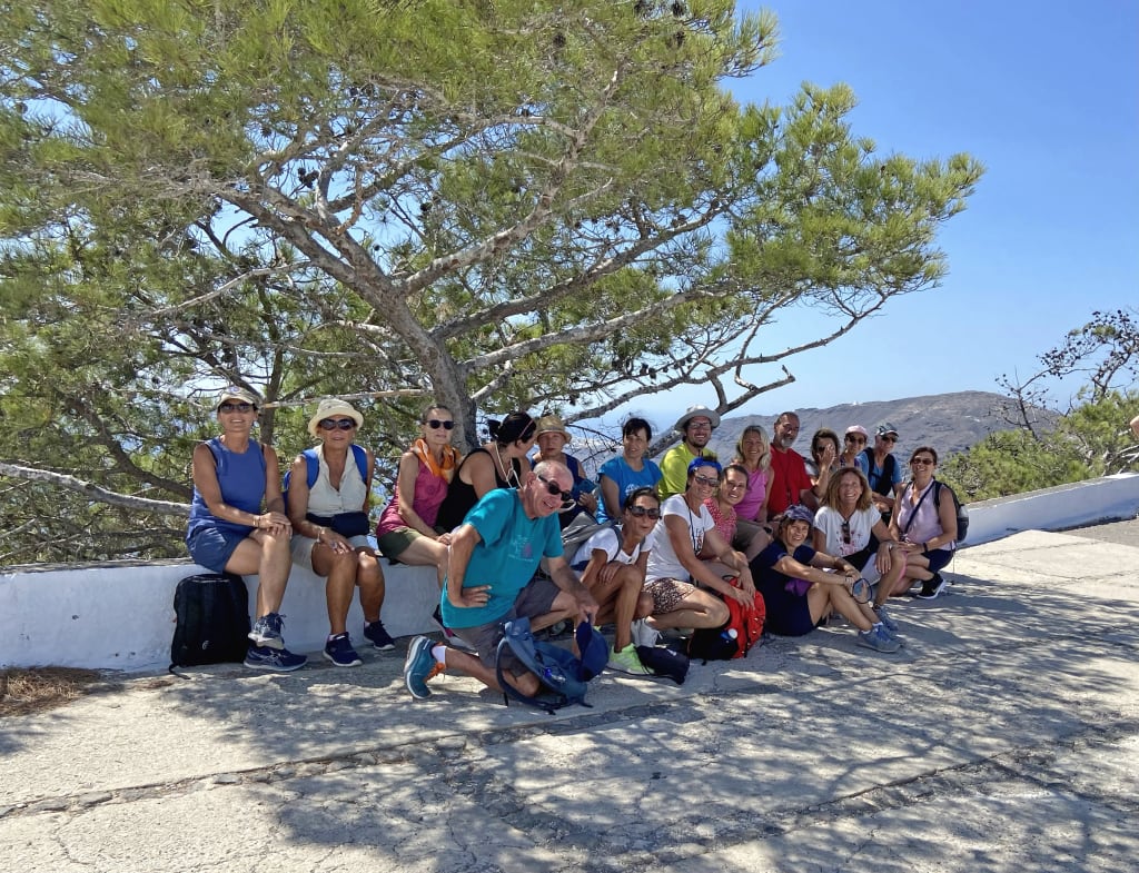 Gruppo di escursionisti che si riposa sotto un albero lungo un sentiero panoramico. Viaggi trekking in gruppo.
