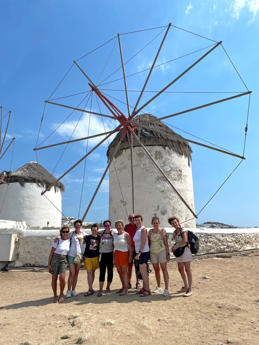 Gruppo in viaggio con "Girolibero" in posa davanti a un mulino a vento tradizionale a Mykonos, Grecia.