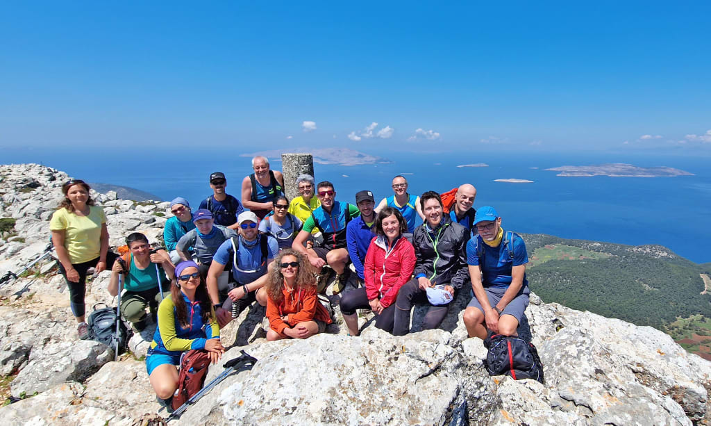 Gruppo di escursionisti in cima al Monte Attavyros, il punto più alto di Rodi, con panorama mozzafiato sull'isola durante un trekking di primavera.