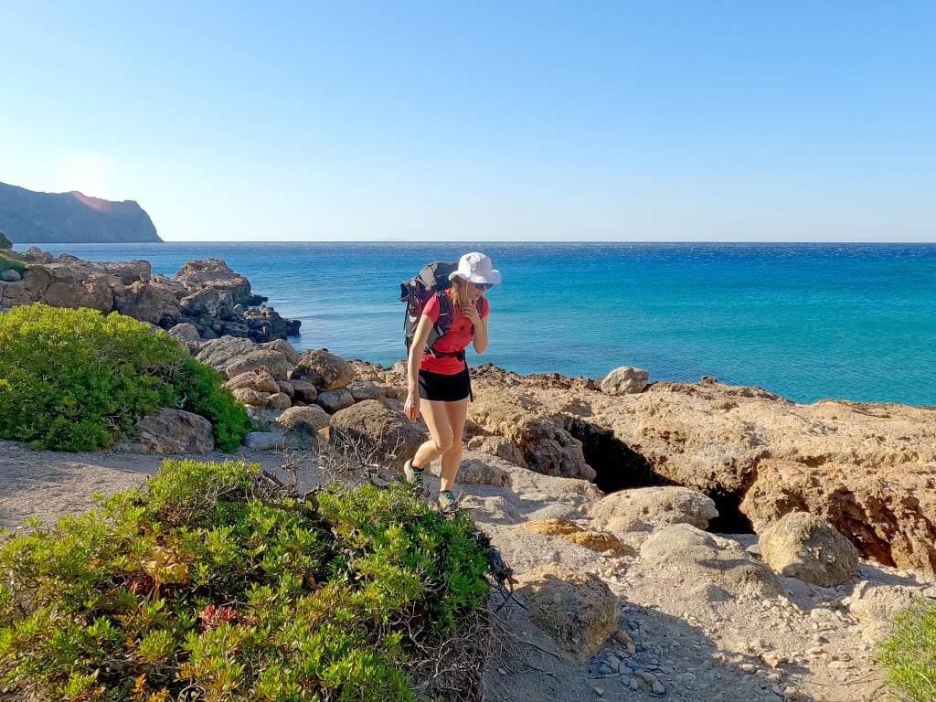 Escursionista in viaggio con Girolibero lungo il sentiero costiero di Creta, Grecia, con vista sul mare cristallino e vegetazione mediterranea.