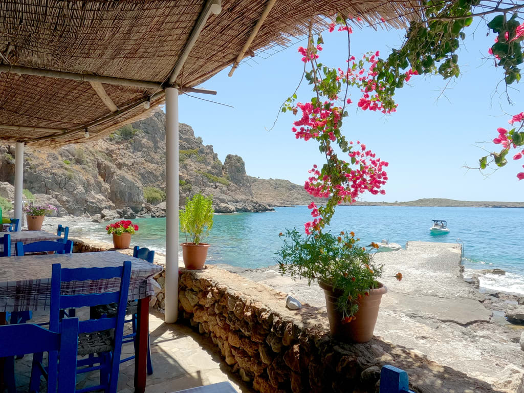 Taverna tradizionale sul mare a Loutro, Creta, Grecia, con tavoli all’ombra e vista panoramica.