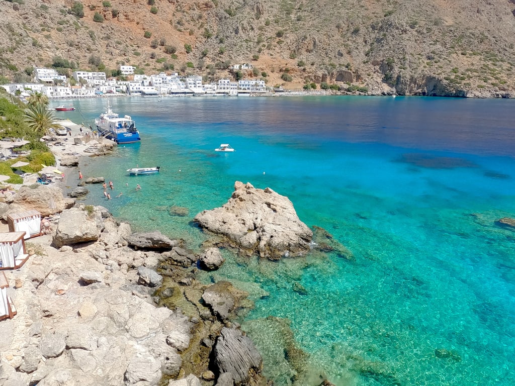 Spiaggia di Glyka Nera a Creta, Grecia, con acqua turchese, rocce e ombrelloni in paglia.