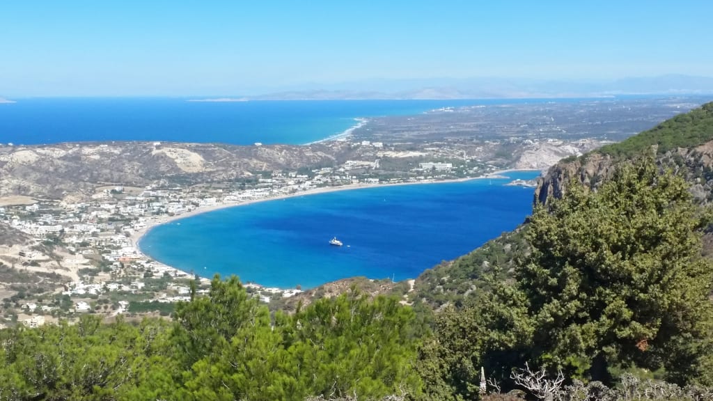 Panoramica sulla Baia di Kefalos con mare cristallino e vegetazione.