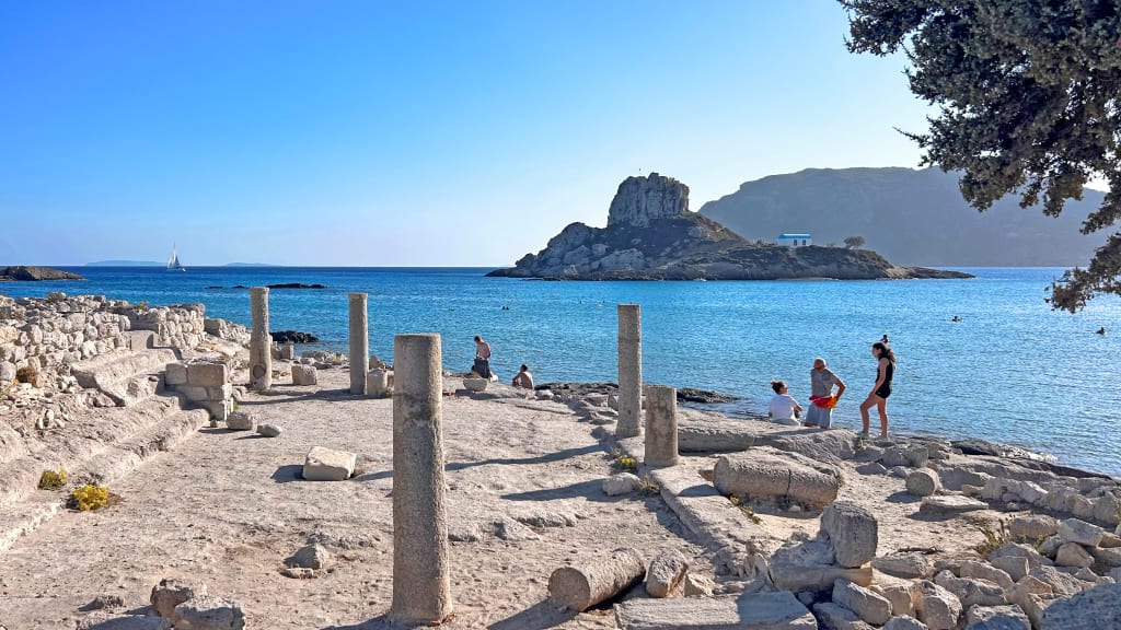 Rovine antiche sulla spiaggia di Kos con colonne e visitatori in esplorazione.