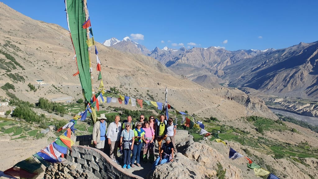 Gruppo di viaggiatori accanto alle bandiere di preghiera buddhiste su un passo di montagna tra Kinnaur e Spiti nell’Himalaya indiano