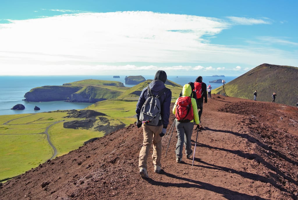 Escursionisti in vacanza con Girolibero che percorrono un sentiero panoramico con vista sull'oceano e sull'arcipelago delle Isole Vestmann, Islanda.