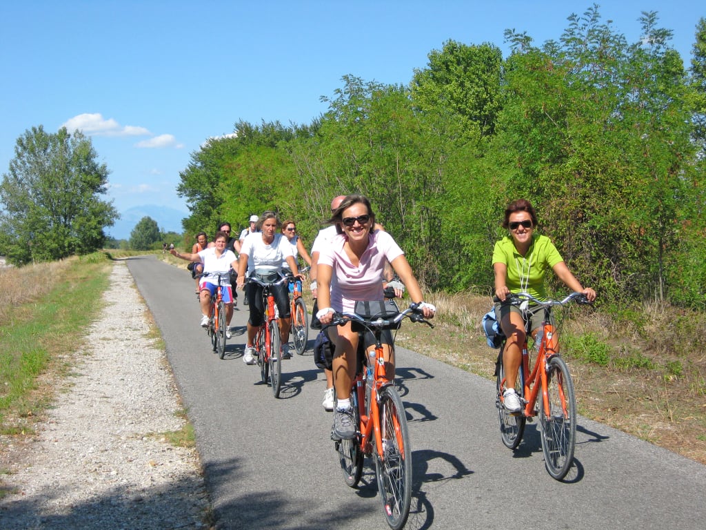 Gruppo di ciclisti su strada di campagna, cicloturismo di gruppo tra paesaggi rurali europei.