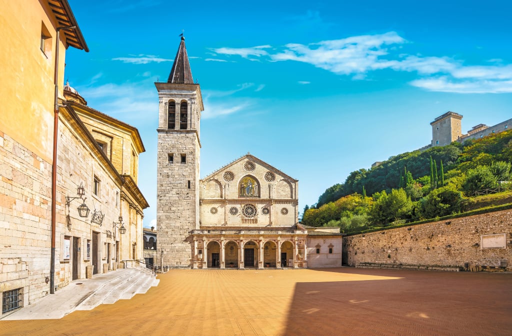 Vista della Piazza del Duomo a Spoleto con la Cattedrale di Santa Maria Assunta e il cielo blu sullo sfondo.