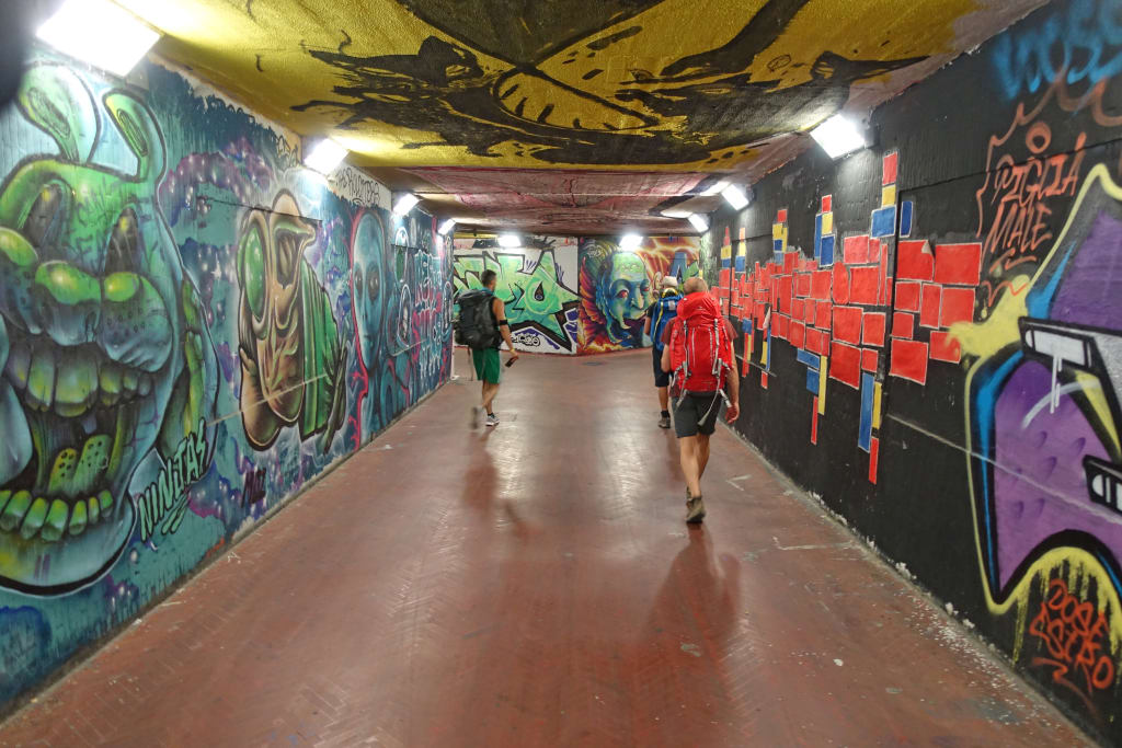 Escursionisti percorrono un sottopassaggio pedonale con graffiti colorati