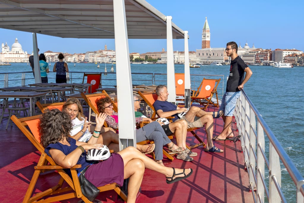 Turisti in barca in relax su sedie a sdraio con vista sul Campanile di San Marco, Venezia.