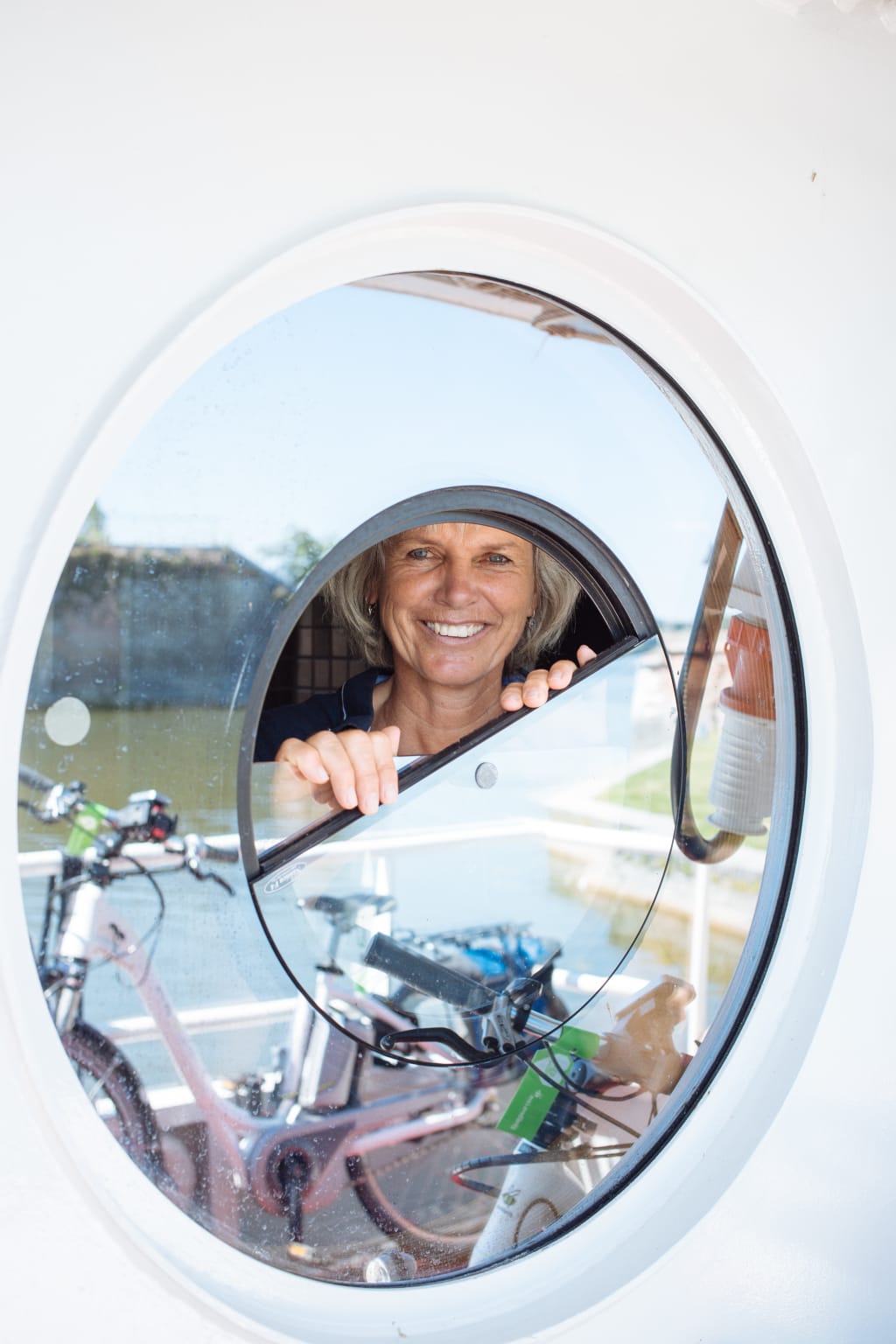 Smiling woman seen through a porthole while arranging her bike on a boat