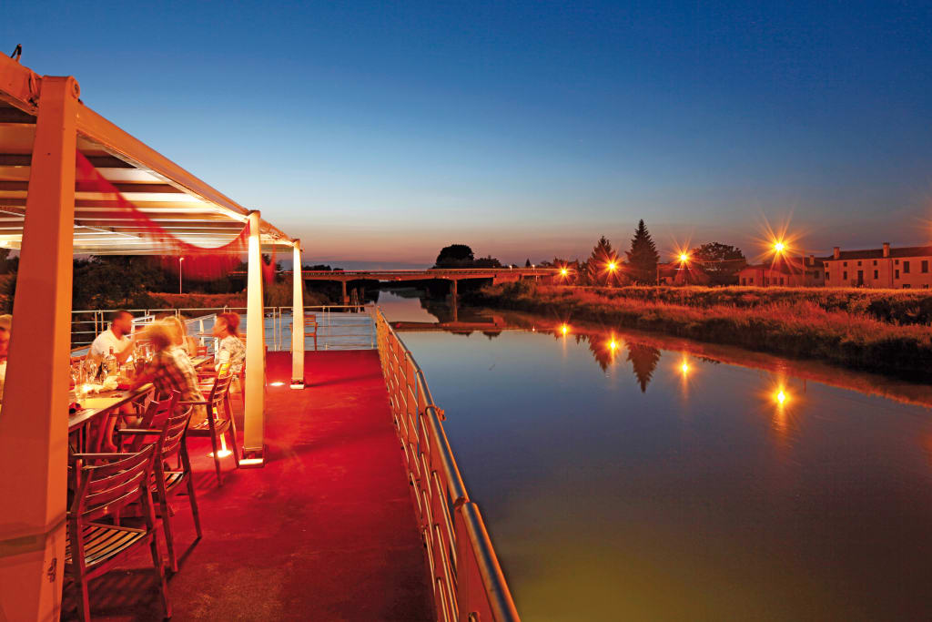 Travellers dining in a boat sailing down the river at night with lights