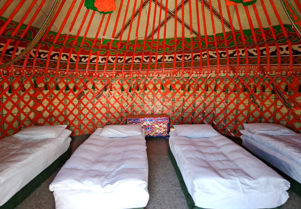 Interno di una yurta tradizionale kirghisa con letti preparati per gli ospiti, decorata con tessuti colorati.