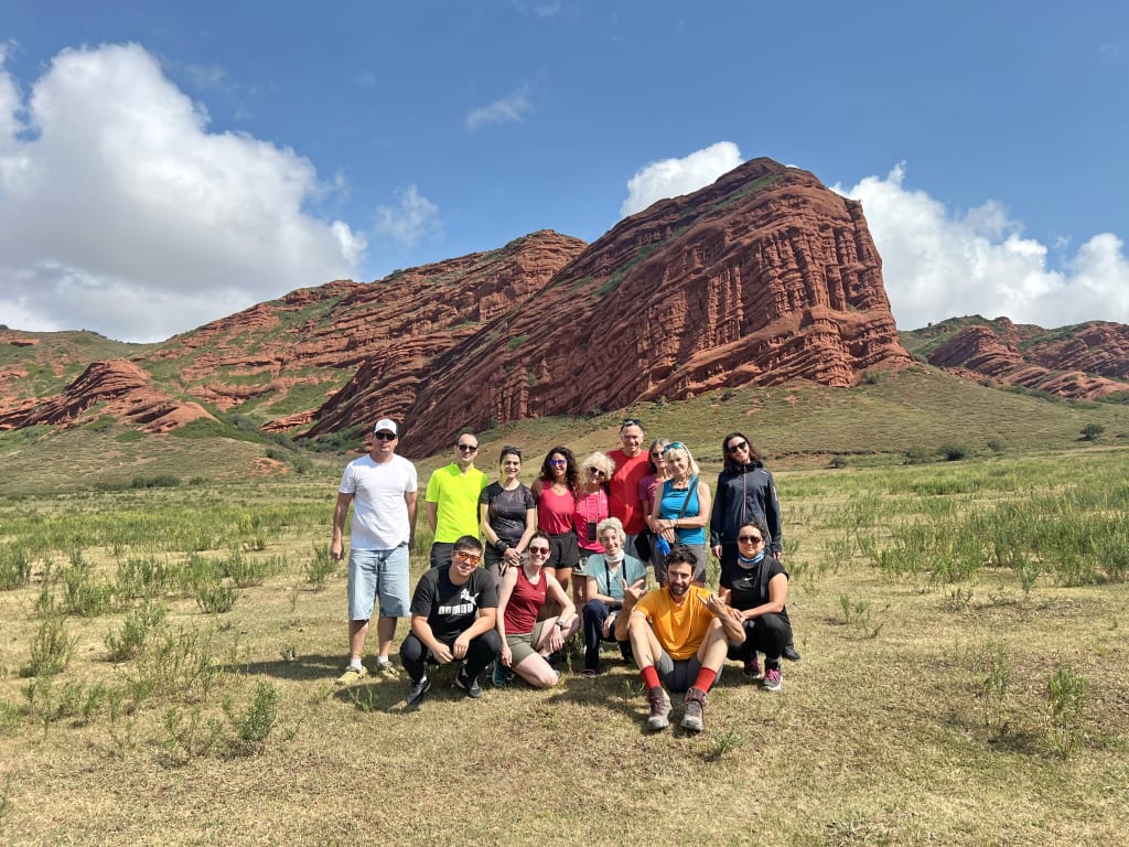 Gruppo di turisti in posa davanti alle rocce rosse di Jeti-Ögüz durante un viaggio di gruppo in Kirghizistan