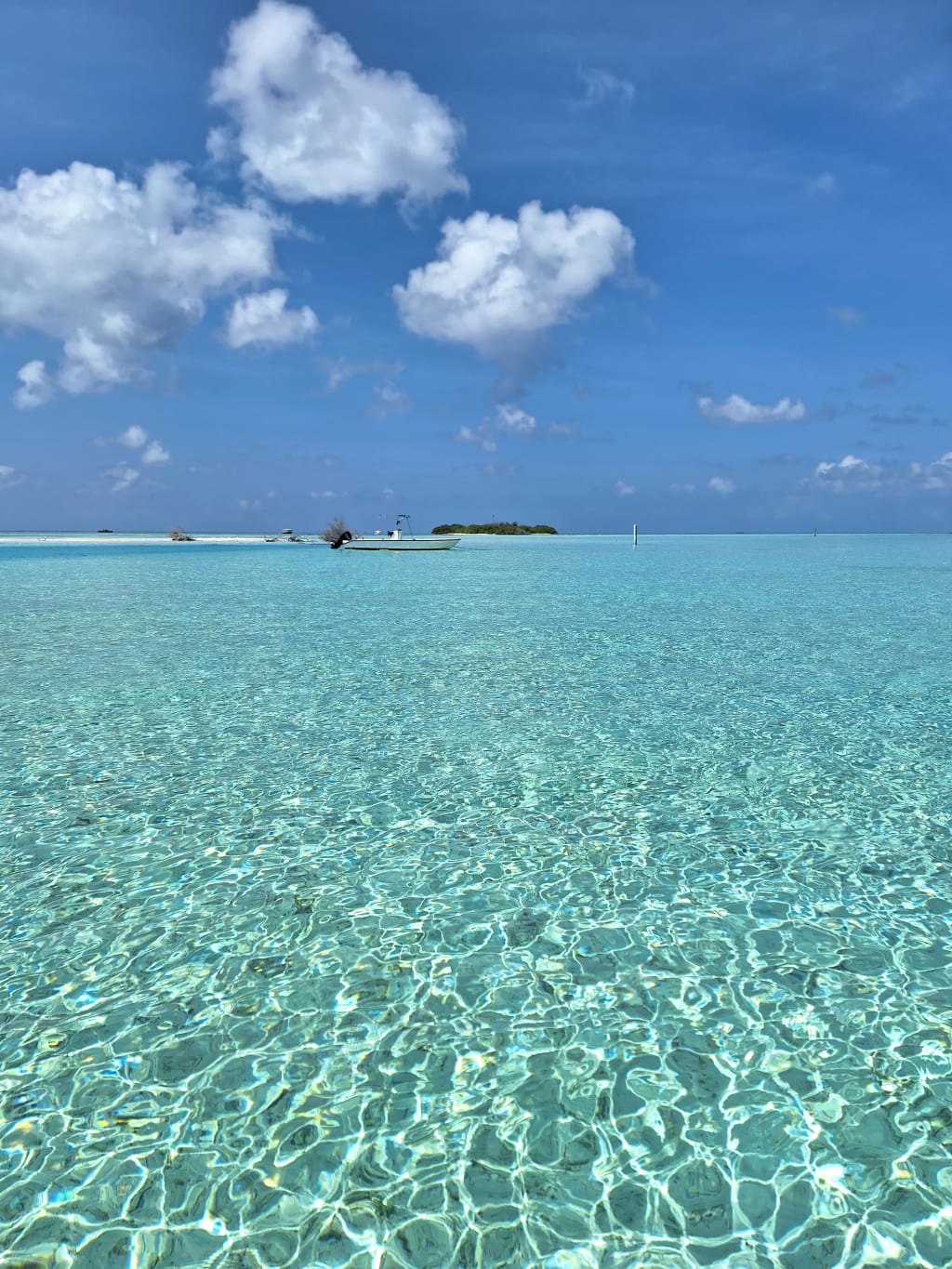 Acqua turchese trasparente su una laguna alle Maldive, con cielo azzurro e nuvole leggere.