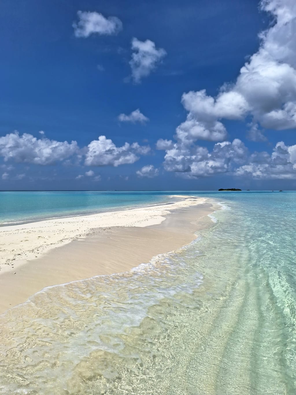 Striscia di sabbia tra acque basse cristalline alle Maldive, cielo azzurro e atmosfera tropicale.