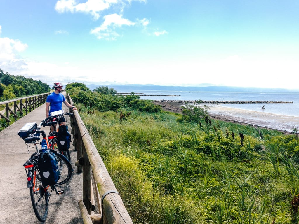 Ciclista fermo su una passerella con vista sul mare lungo la ciclovia adriatica