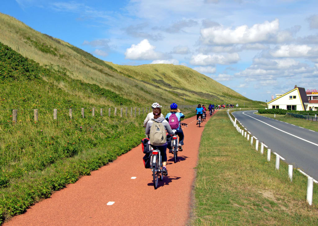 Ciclisti su una pista pavimentata rossa vicino a colline verdi, vacanze in bicicletta "Girolibero"