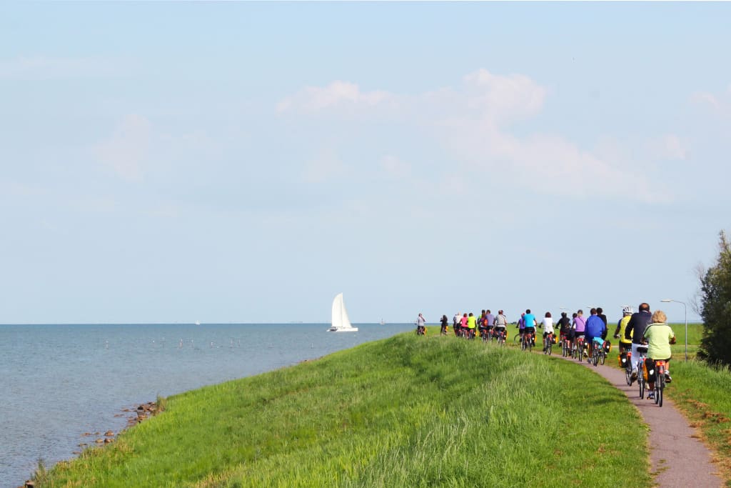Gruppo di ciclisti in viaggio con "Girolibero" lungo una diga con vista sul lago IJsselmeer, Olanda. Vacanze in bici e barca