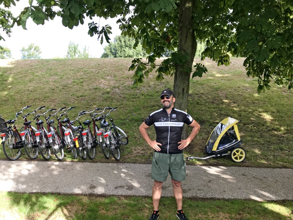 Uomo con varie biciclette parcheggiate su una collina verde, percorso ciclabile in Olanda.