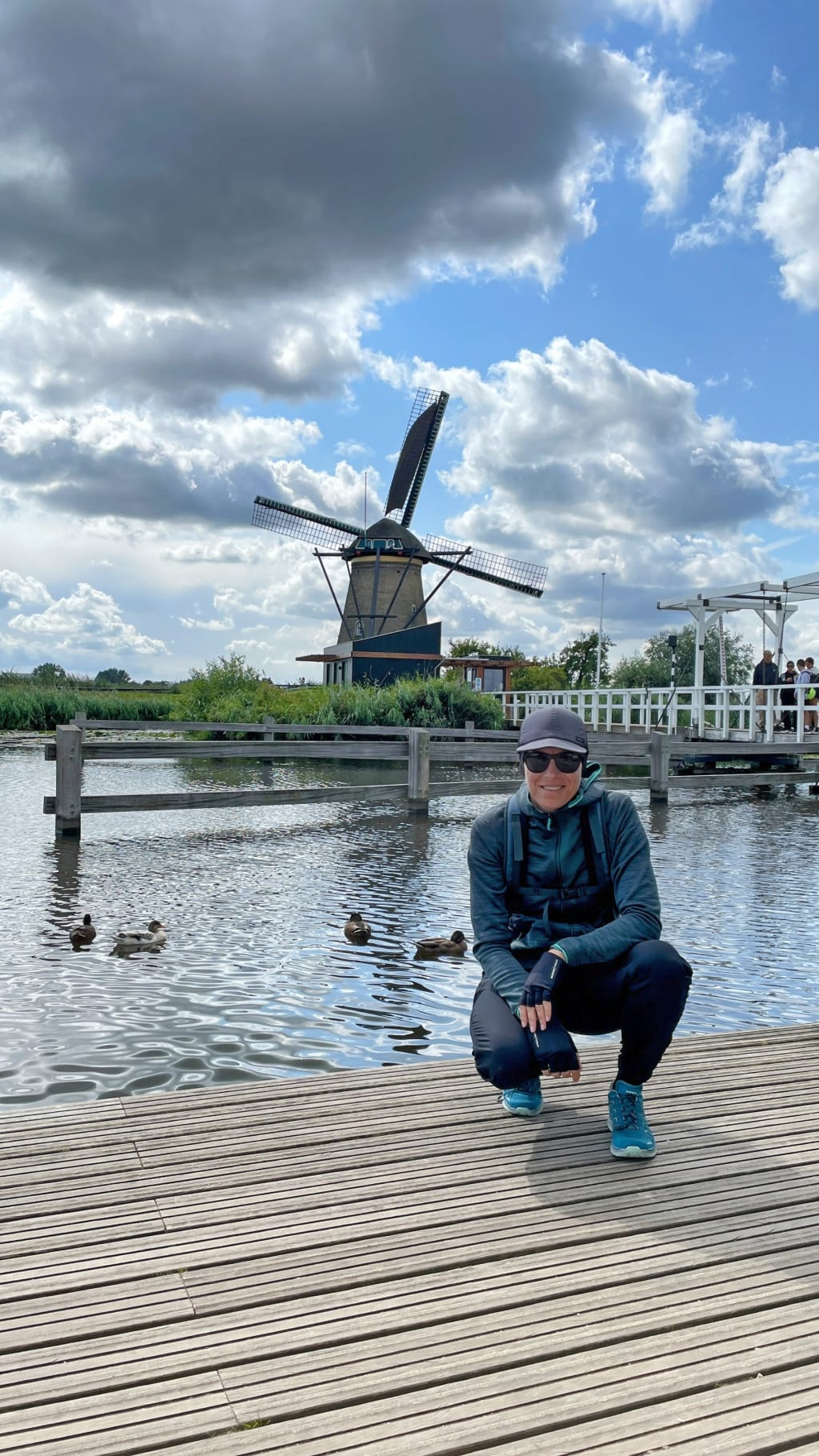 Turista in posa con vista su un canale con mulino a vento e paesaggio verde, Amsterdam