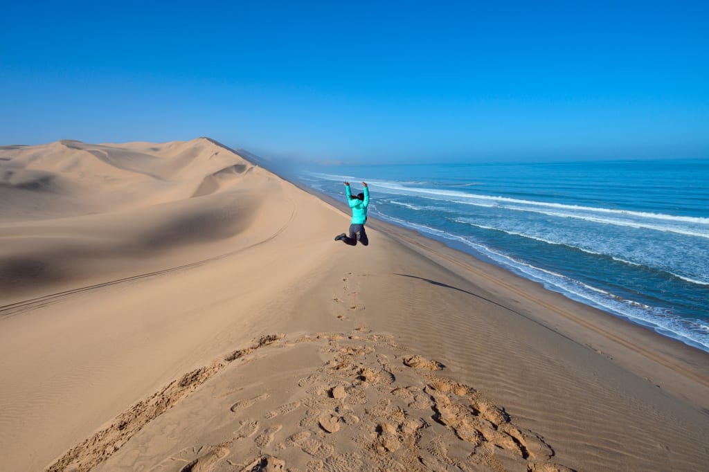 Turista in posa lungo una costa sabbiosa che si estende verso l'oceano.