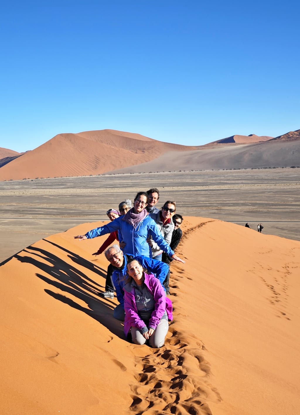 Gruppo in viaggio in Africa con "Girolibero" in posa su una duna di sabbia sotto il sole in Namibia.