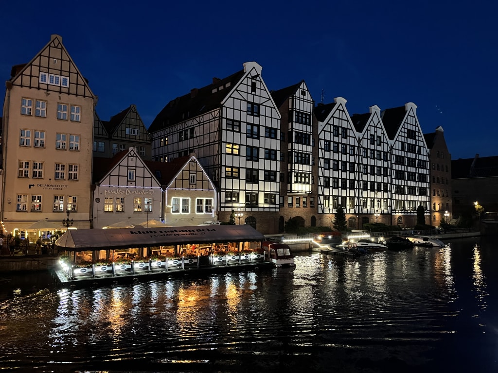 Canale illuminato di notte con edifici storici lungo la riva a Danzica, Polonia.