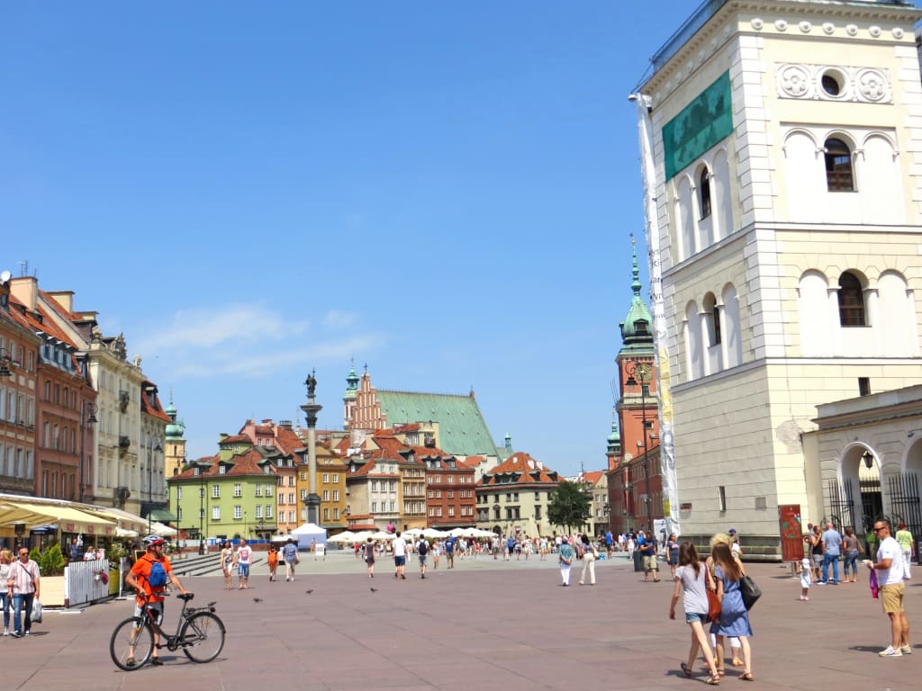 Castello reale e Chiesa di Sant'Anna nella piazza del Castello a Varsavia con ciclisti e turisti