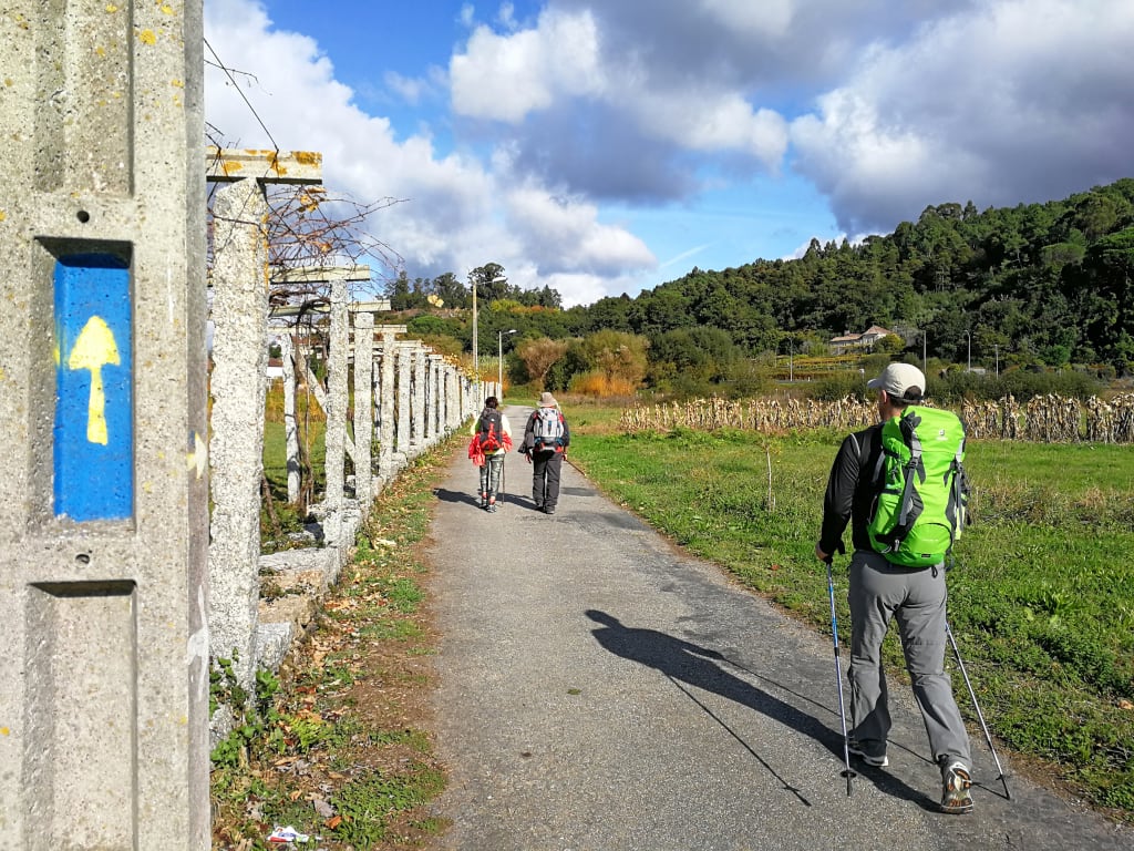 Pellegrino che segue il segnale blu del Cammino di Santiago lungo un antico muro di pietra in Portogallo.