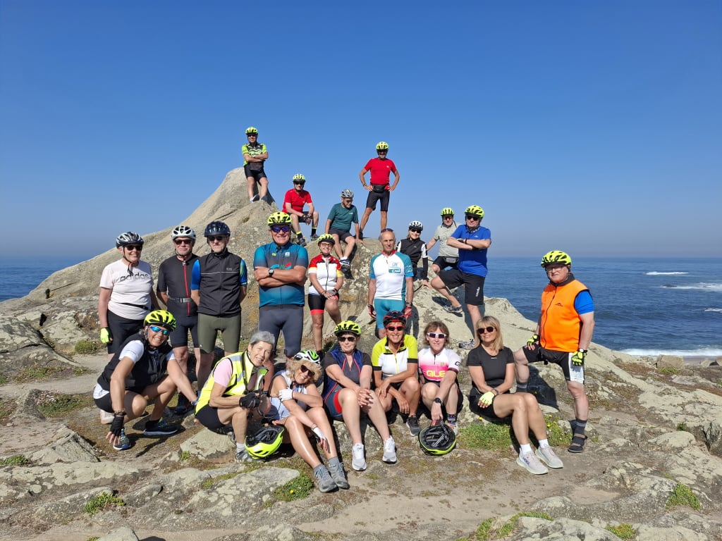 Gruppo di viaggiatori seduti sugli scogli dell’oceano Atlantico lungo la costa della Galizia durante un viaggio in bici sul Cammino di Santiago