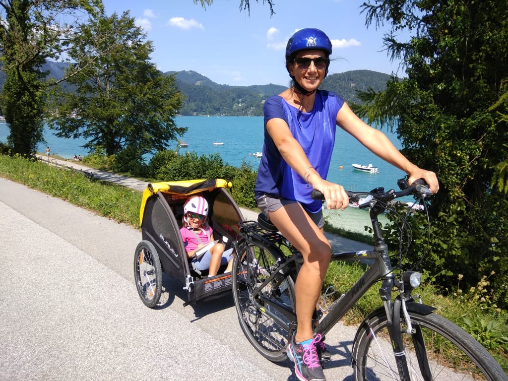 Vacanze in bici, mamma con bambino in bicicletta in riva al lago