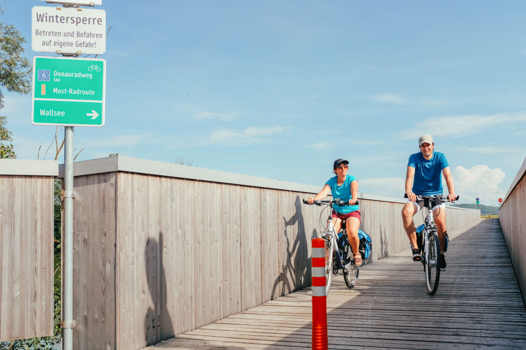 Ciclisti in viaggio con Girolibero attraversano un ponte di legno lungo il percorso ciclabile del Danubio, Austria.