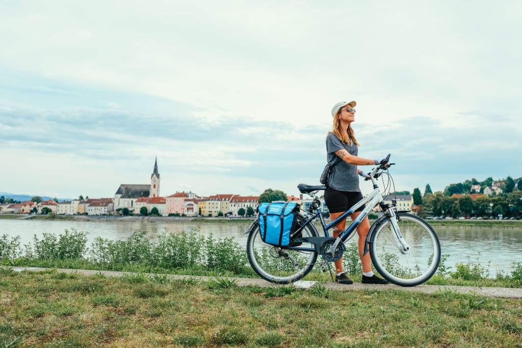 Ciclista davanti al fiume Danubio con sullo sfondo un villaggio caratteristico in Austria