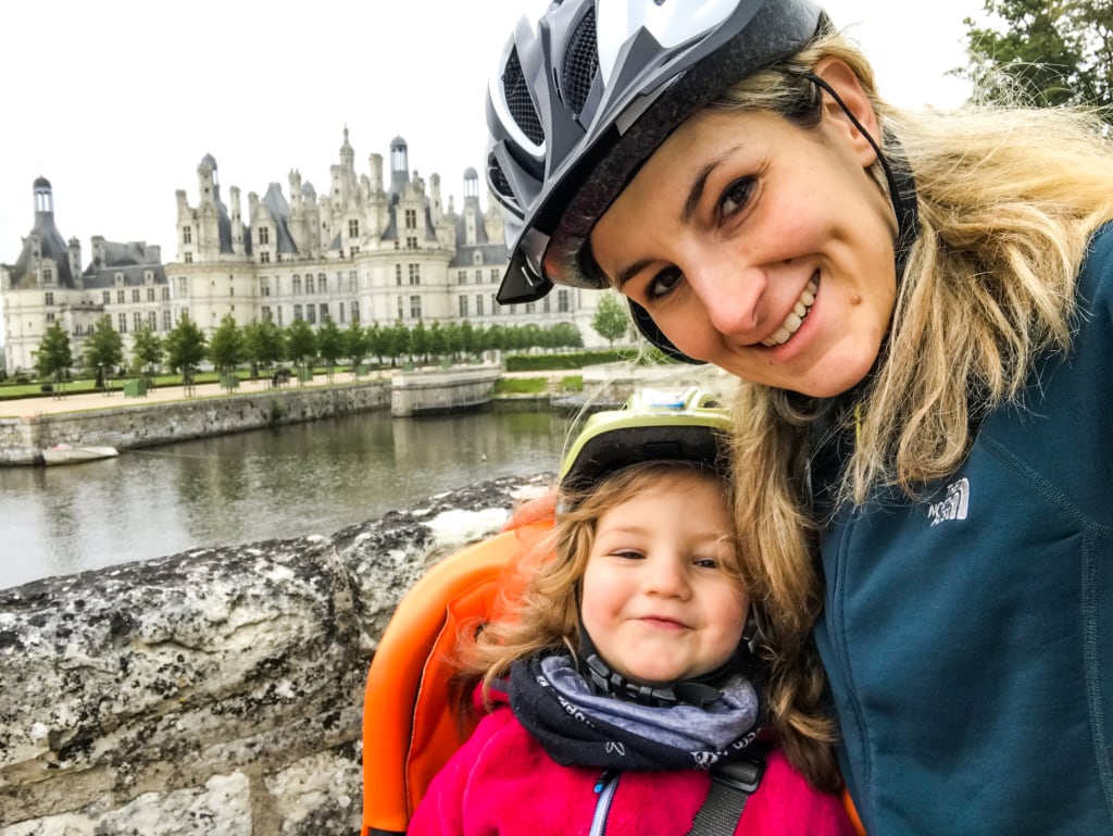 Lächelnder Radfahrer mit kleinem Mädchen auf dem Fahrrad entlang der Loire, vor dem Schloss Amboise, Familienradreise