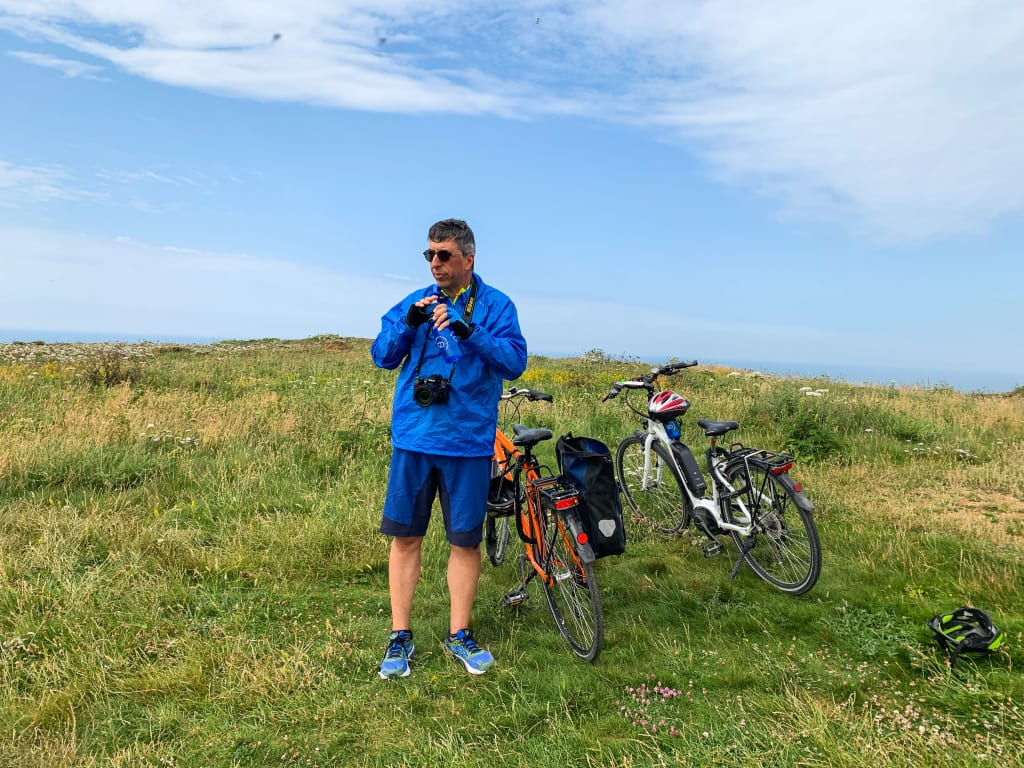 Da Parigi a Londra Velia Freni. Ciclista con bicicletta su un sentiero erboso, circondato dalla natura e dal cielo azzurro.