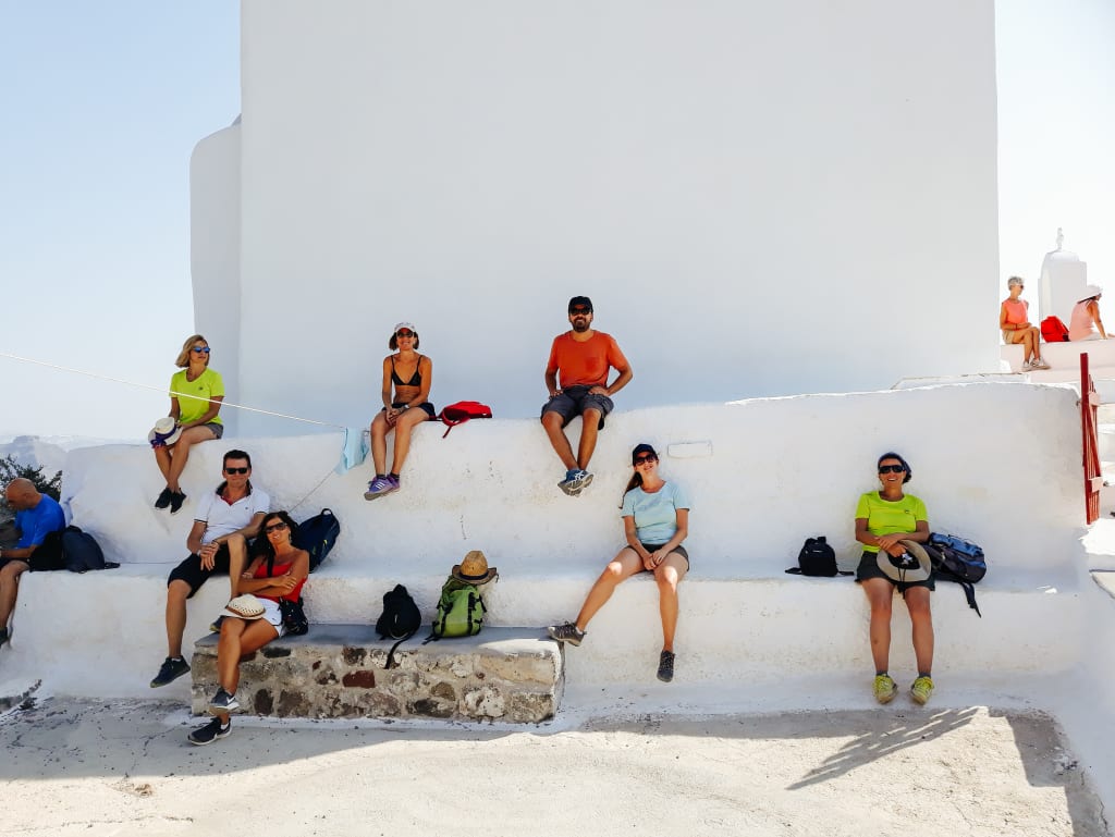 Turisti che si riposano sui gradoni di un muro bianco di Oia a Santorini in viaggio con "Girolibero", vacanze di gruppo in Grecia