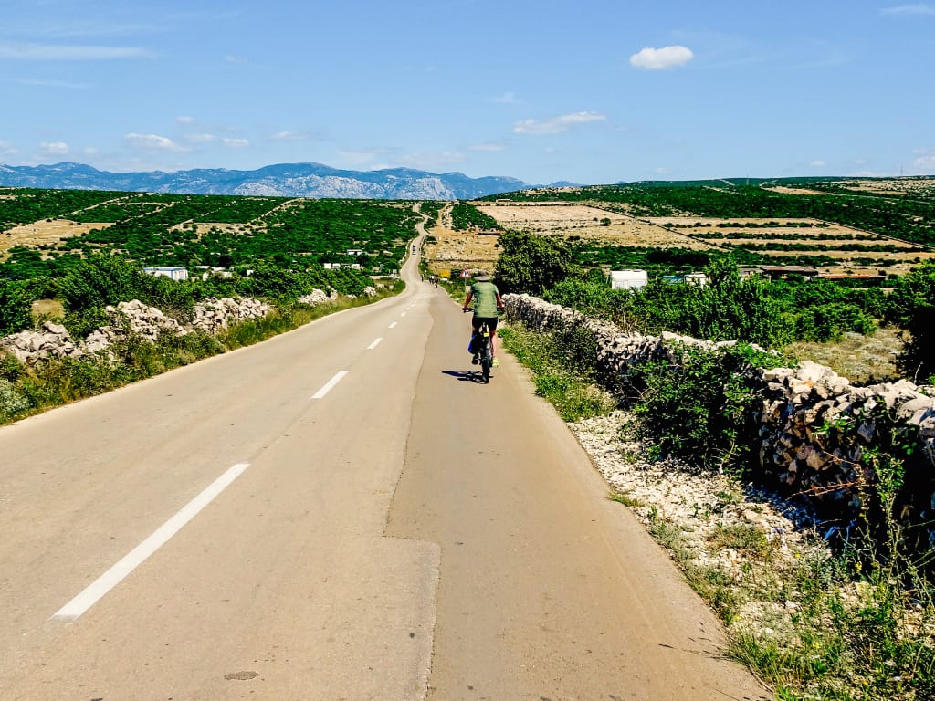Cyclist along a scenic coastal road with views of the sea and mountains, Dalmatia